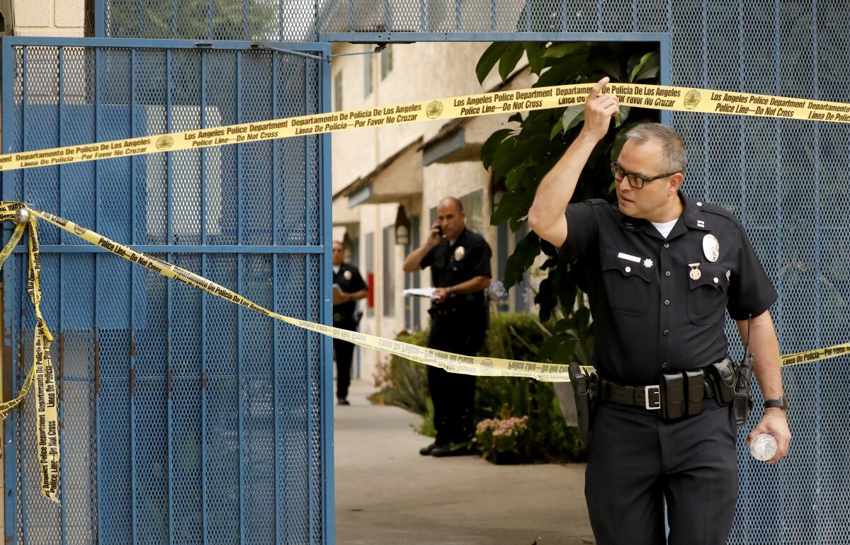 A police officer lifts crime scene tape from an apartment complex