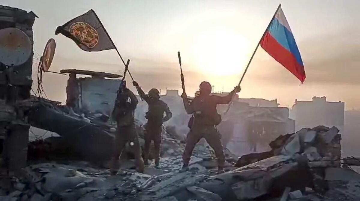 People in fatigues wave flags while standing on the rubble of a building.