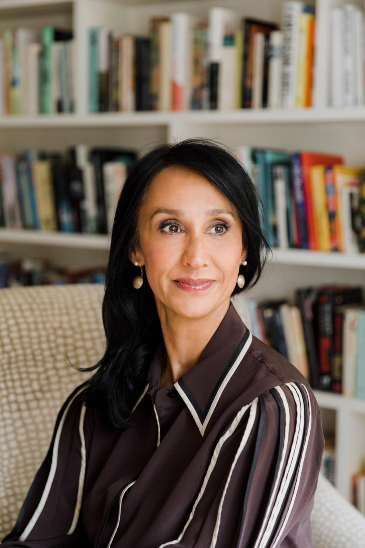 A woman seated in front of full bookshelves.