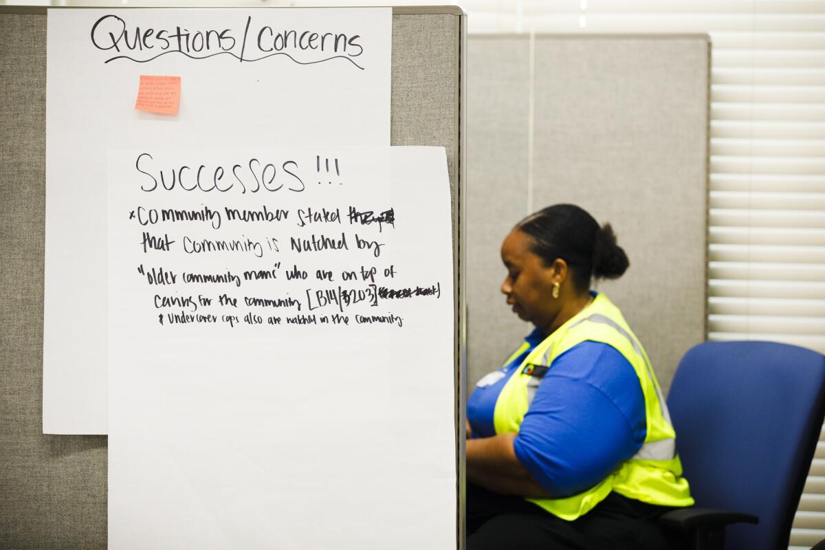 A woman works in an office where a poster outlining "successes" hangs on a cubicle wall. 