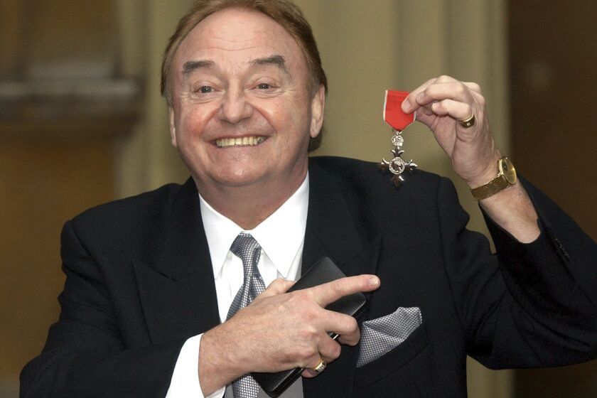 FILE - In this Dec. 12, 2003 file photo, Gerry Marsden holds his MBE. Gerry Marsden, the British singer and lead singer of Gerry and the Pacemakers, who was instrumental in turning a song from the Rodgers and Hammerstein musical “Carousel” into one of the great anthems in the world of football, has died. He was 78. (Matthew Fearn/PA via AP, File)
