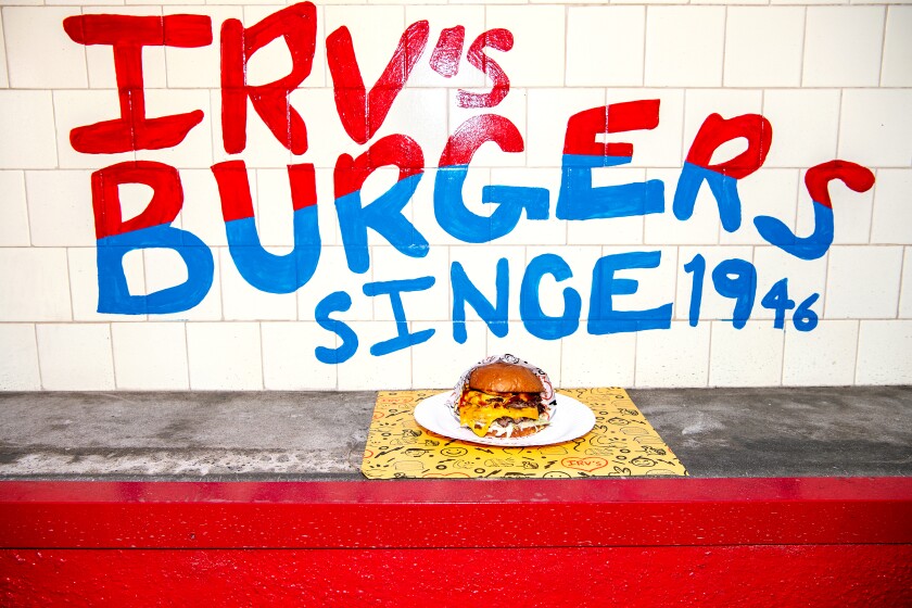 A wall with writing that says Irv's Burgers since 1946 and, in foreground, a hamburger