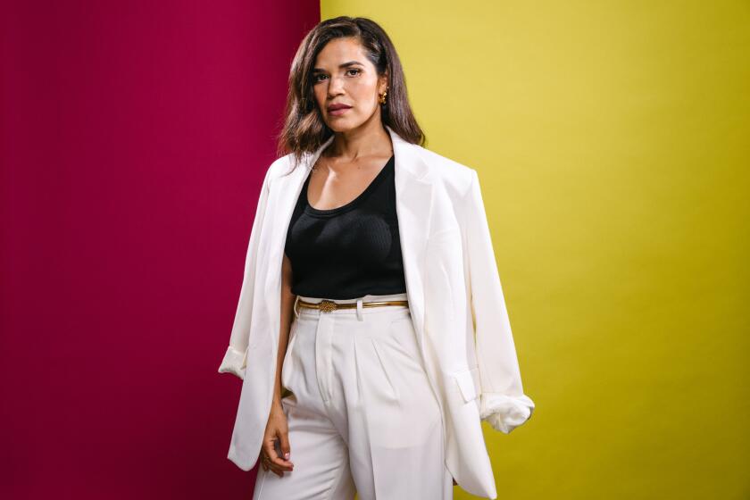 America Ferrera poses in front of a red and yellow background wearing a casual white suit and black scoop-neck shirt