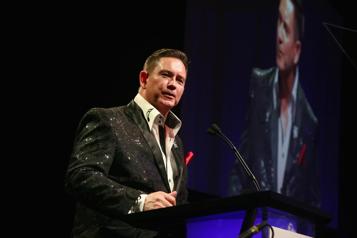 A man speaks on stage with his image on a large screen behind him