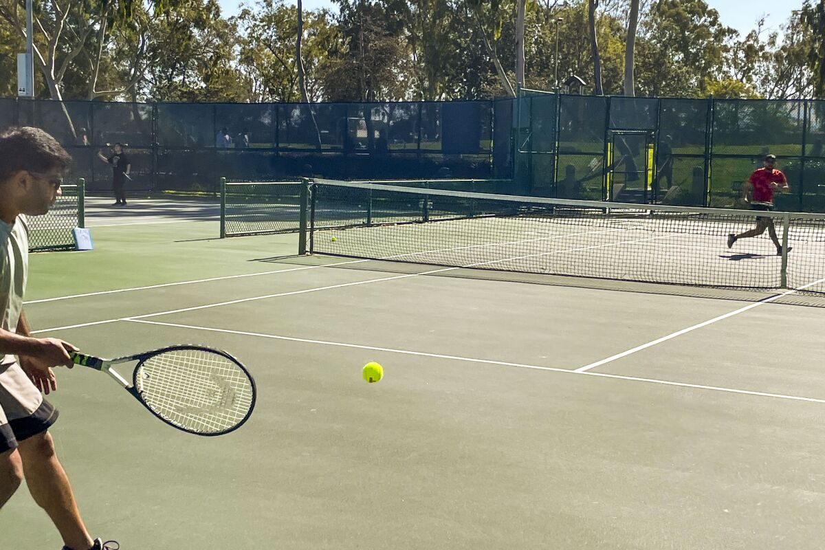 Two people play tennis on a green tennis court