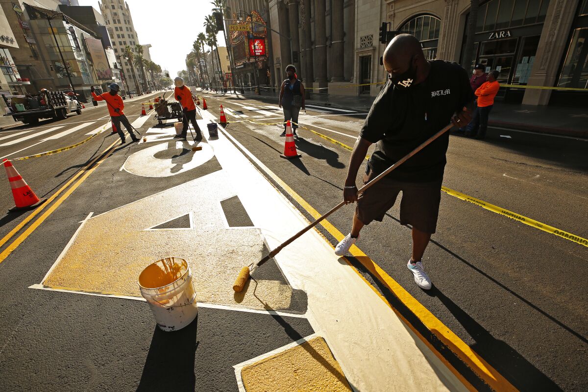 Designer Lucky Alexander Fuller rolls yellow paint down on the first letters of the permanent "All Black Lives Matter."