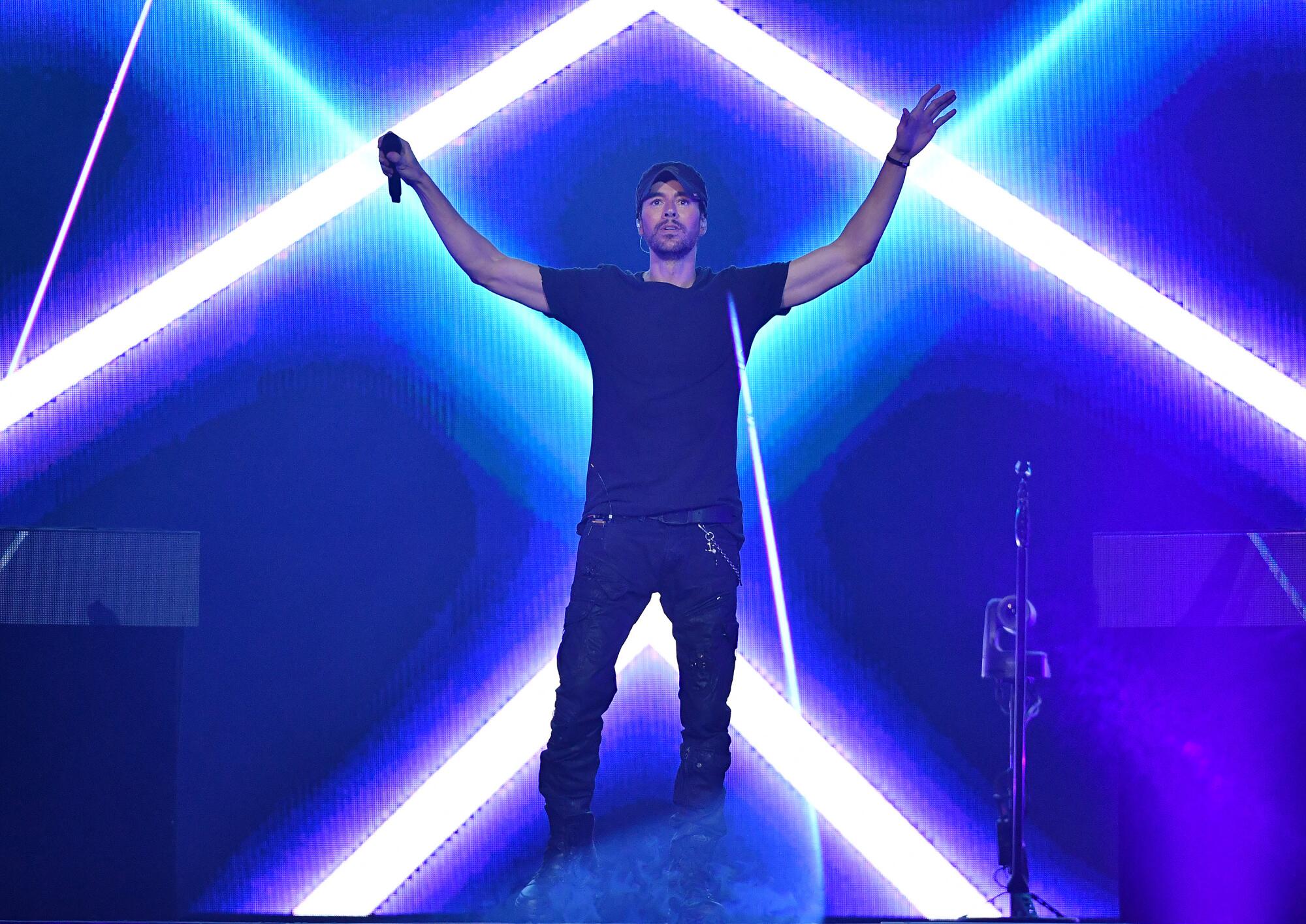 A man holds out his arms in front of shafts of light on stage.