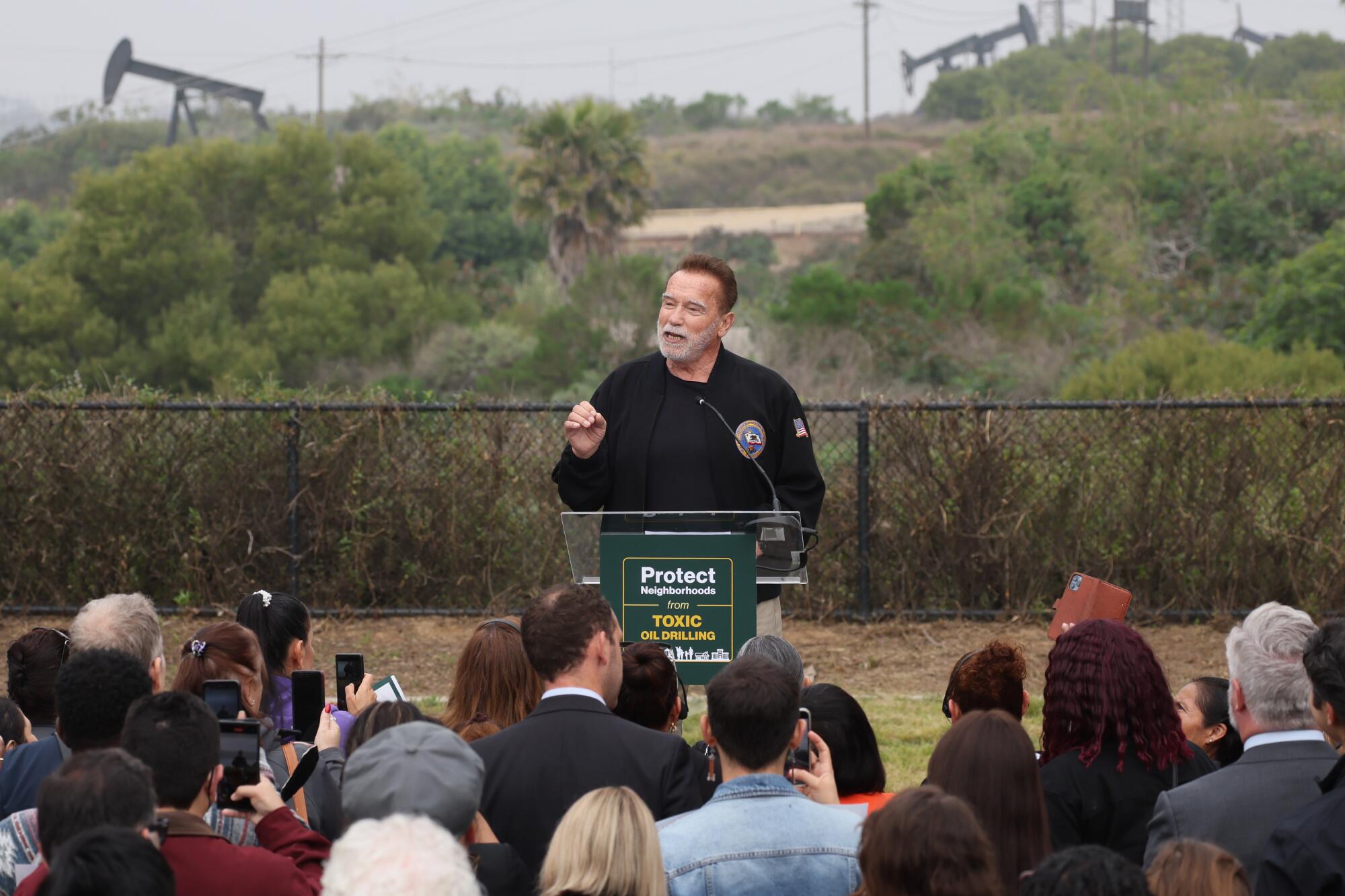 Former California Gov. Arnold Schwarzenegger speaks outdoors while oil pumpjacks are in the background.