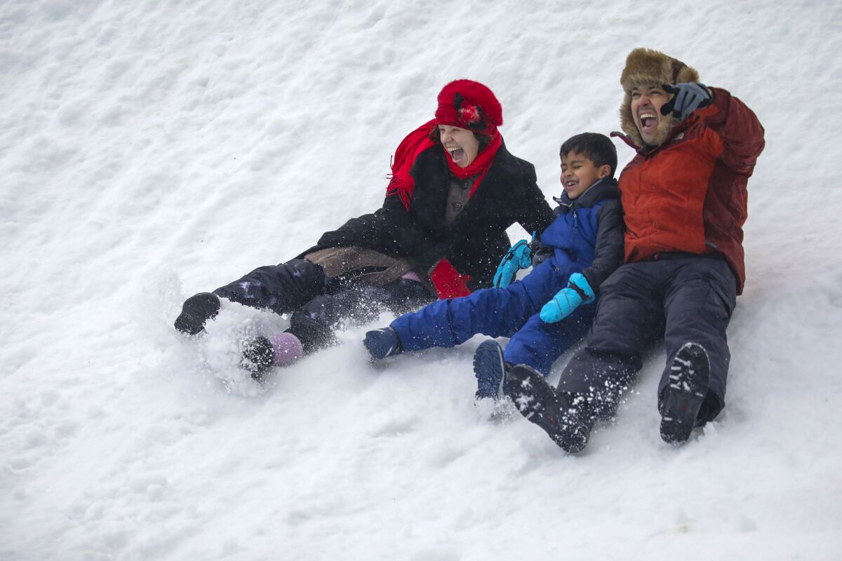 A man, woman and child slide down a snowy hill.