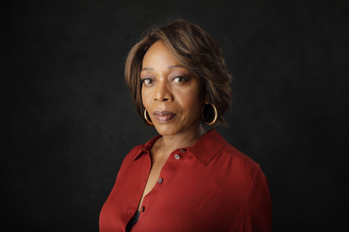 A portrait of Alfre Woodard wearing gold hoop earrings and a red shirt