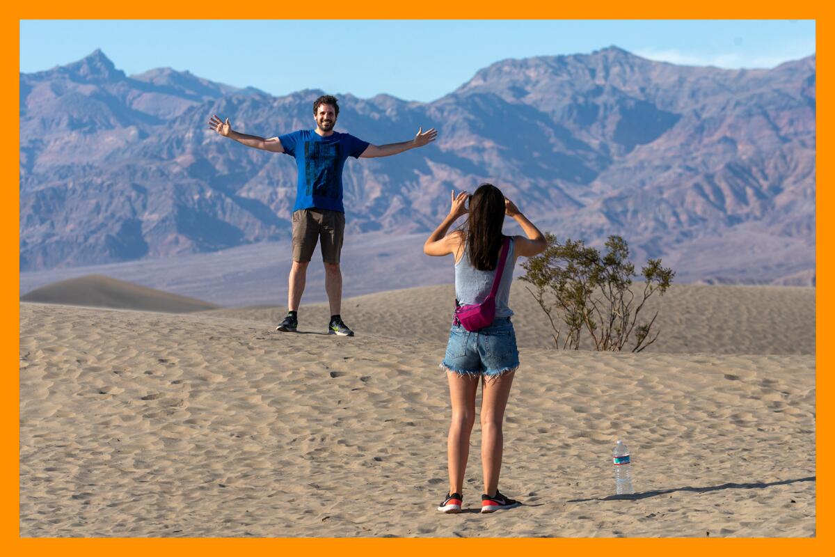 One person photographs another person who is standing in a desert with their arms spread wide