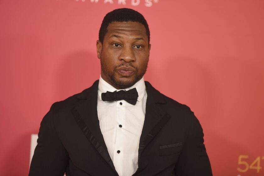 Jonathan Majors wearing a black tuxedo and bowtie against a pink background