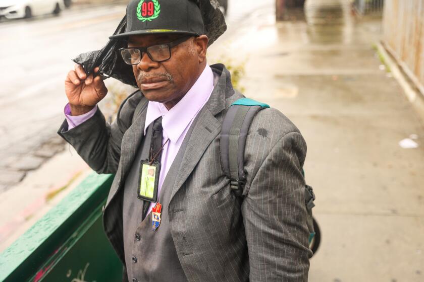 Los Angeles, CA - March 23: Morris Broaster puts a black plastic bag over his head to cover himself from the rain as he waits for the bus on Saturday, March 23, 2024 in Los Angeles, CA. (Michael Blackshire / Los Angeles Times)