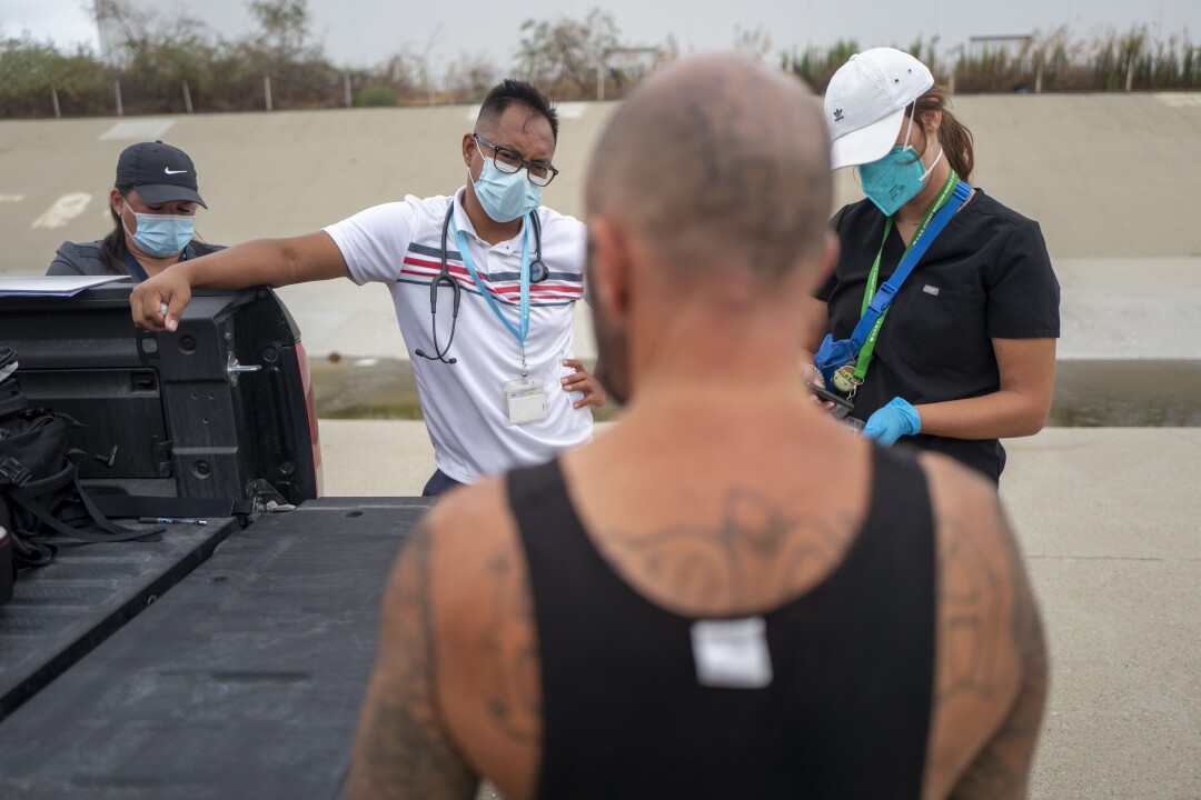 Three people in masks stand on one side of a pickup truck bed talking to a man on the other side.