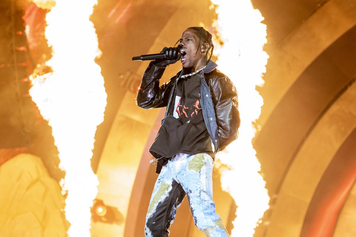 A rapper holding a microphone and performing onstage in front of flames
