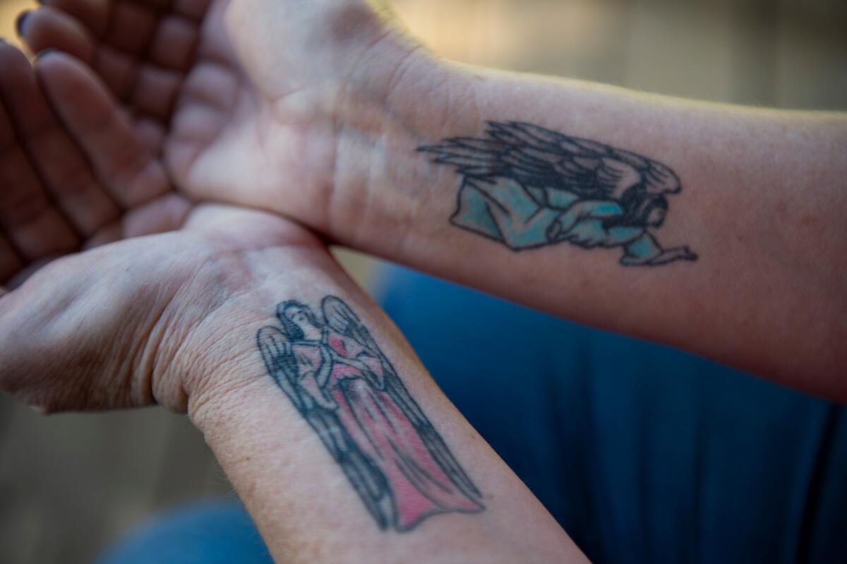 A horizontal frame of two arms, pressed together at palms, facing up, with a tattoo of an angel on each forearm. 