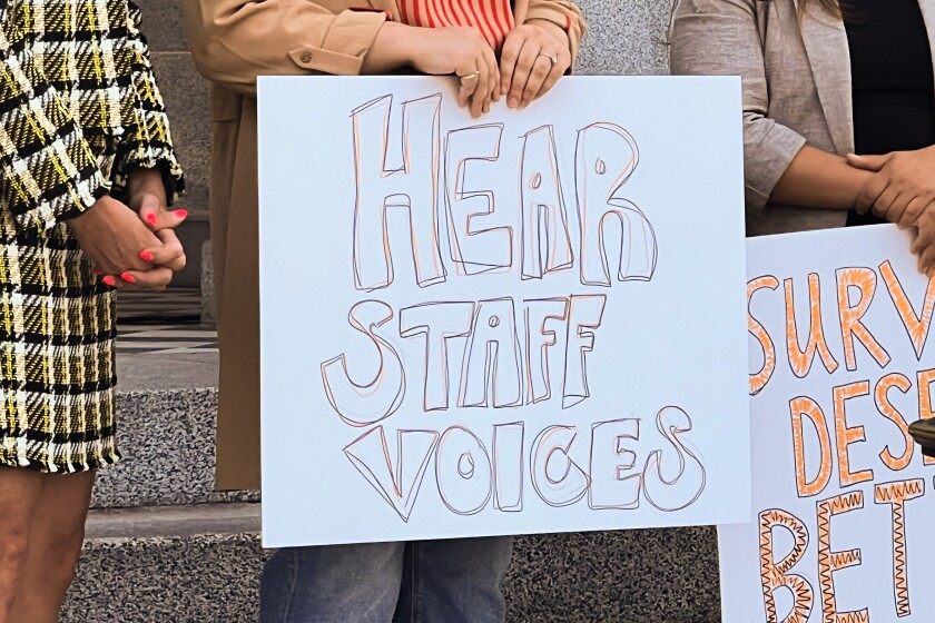 Hands holding a sign that says, "Hear Staff Voices."