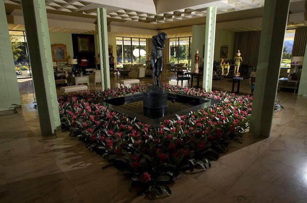 Front doors open to a lofty atrium with its centerpiece, the Auguste Rodin sculpture "Eve," surrounded by pink bromeliads. She is still surrounded by sitting areas with original furniture designed by Haines and Graber in the Hollywood Regency style, as well as the Annenbergs' fine and decorative art.