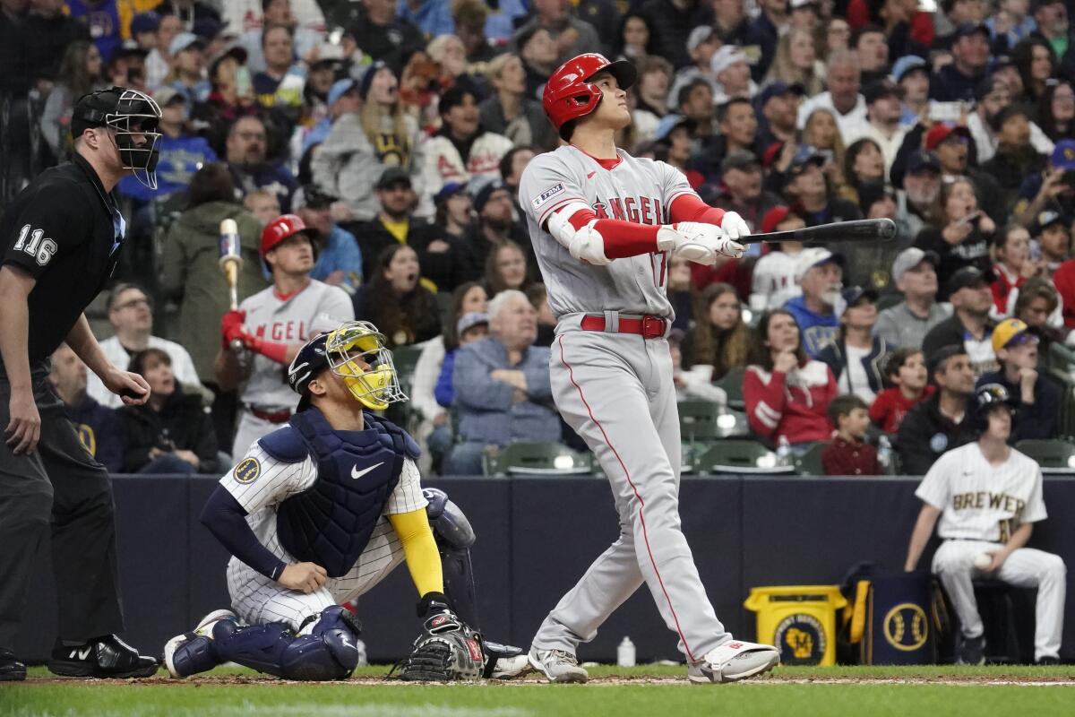 A man in a red helmet holds a baseball bat while watching a hit during a game.