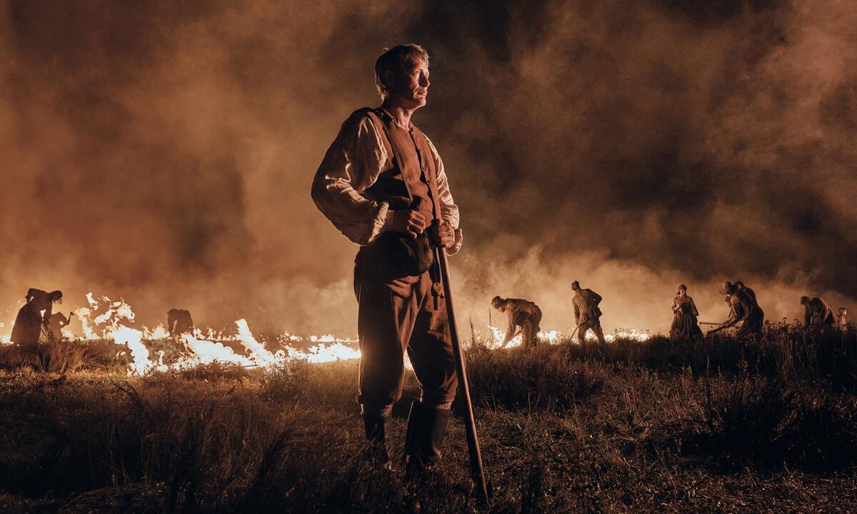 A man stands on a burning field at night.