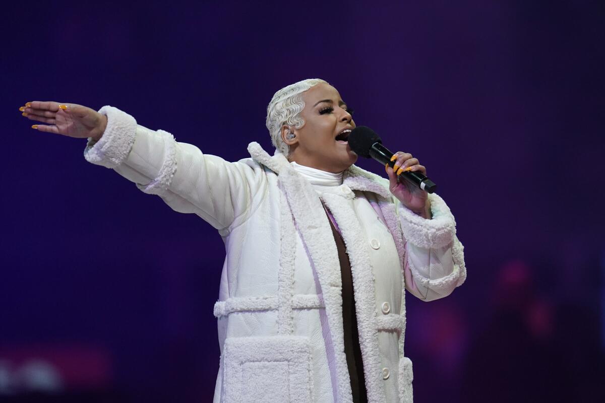 Bobbi Storm sings while raising her hand and wearing a white fur-trimmed coat