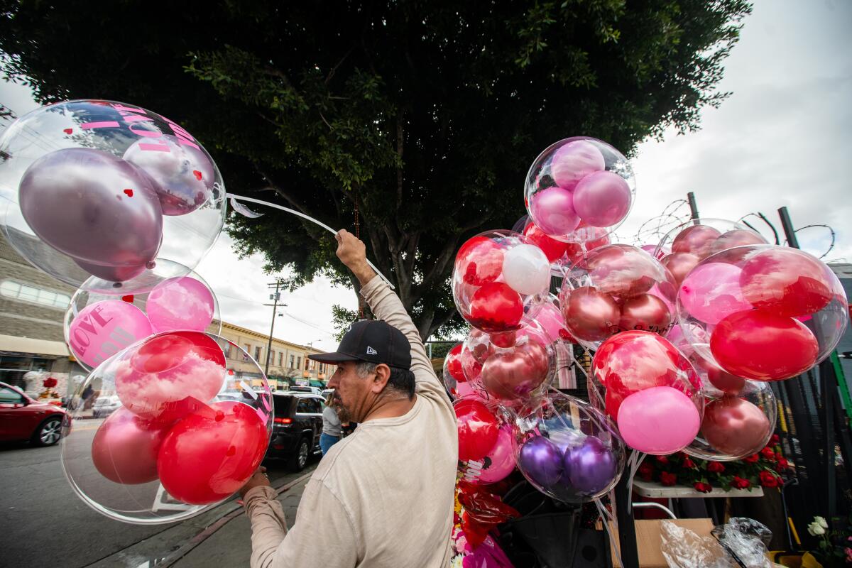 A man stands in the middle, holding red and pink balloons, with more balloons tied to his other side.