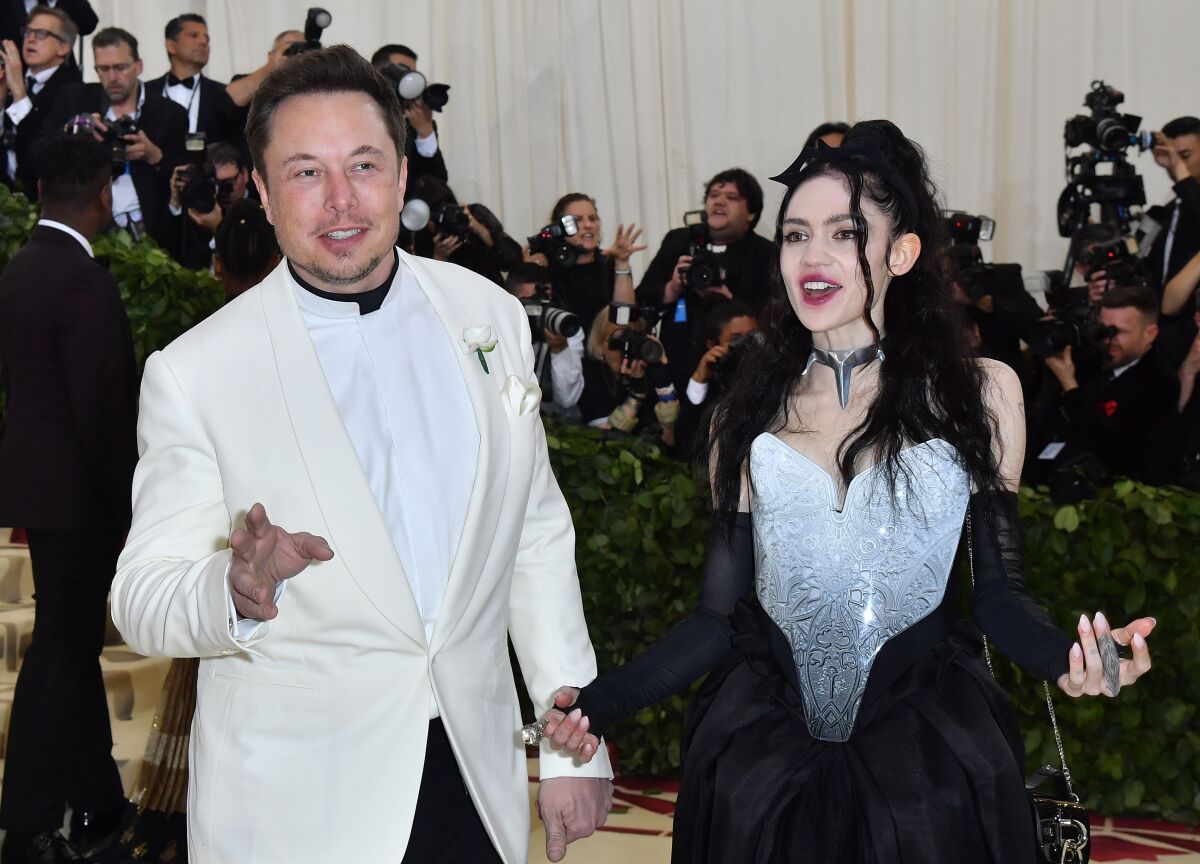 A man in a white tuxedo jacket and woman in a black-and-white gown pose for photographers