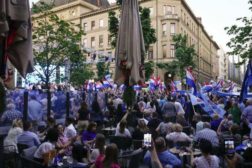 People sit on a cafe terrace while others wave flags during a rolling HDZ party rally in downtown Zagreb, Croatia, Sunday, April 14, 2024. Croatia this week holds an early parliamentary election following a campaign that was marked by heated exchanges between the country's two top officials, creating a political crisis in the Balkan country, a European Union and NATO member state. (AP Photo/Darko Bandic)