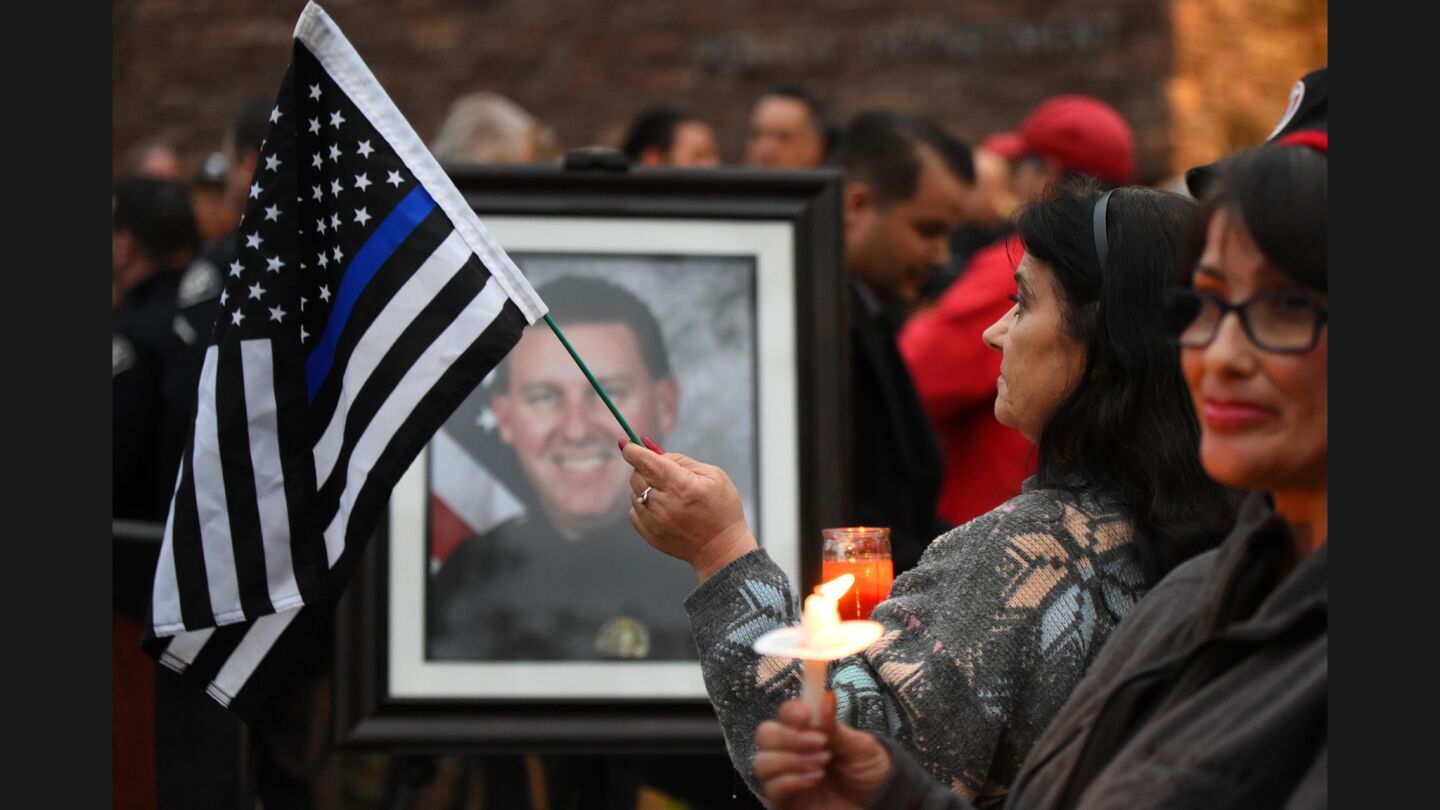 Joanne Carrel holds a black and white American flag by a picture of slain Whittier police officer Keith Boyer during a vigil at the Whittier police station.