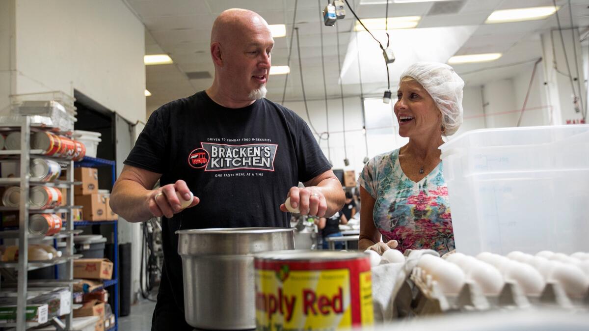 Bill Bracken, founder of Bracken's Kitchen, shows volunteer Krista Koch how to crack eggs with one hand at Hana Kitchens in Huntington Beach on Sept. 5.