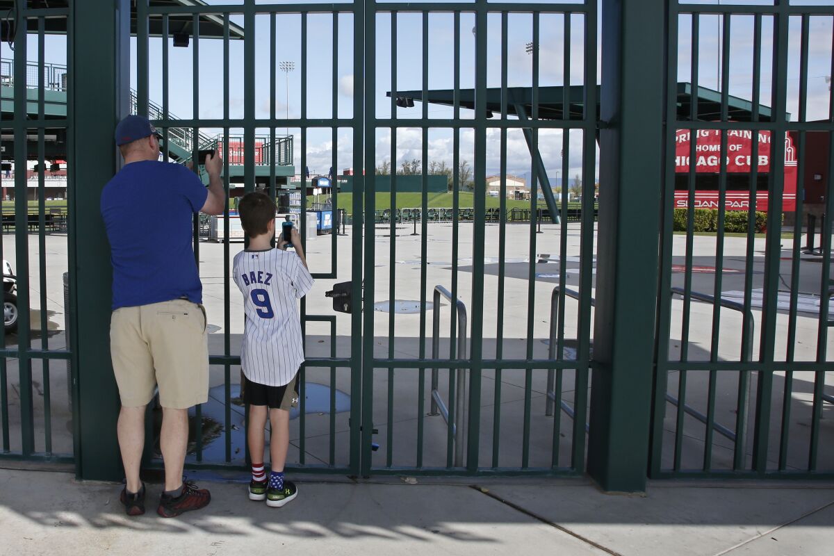 Cubs fans take photos through locked gates at Sloan Park, the spring training site of the Chicago Cubs, in Mesa, Ariz.