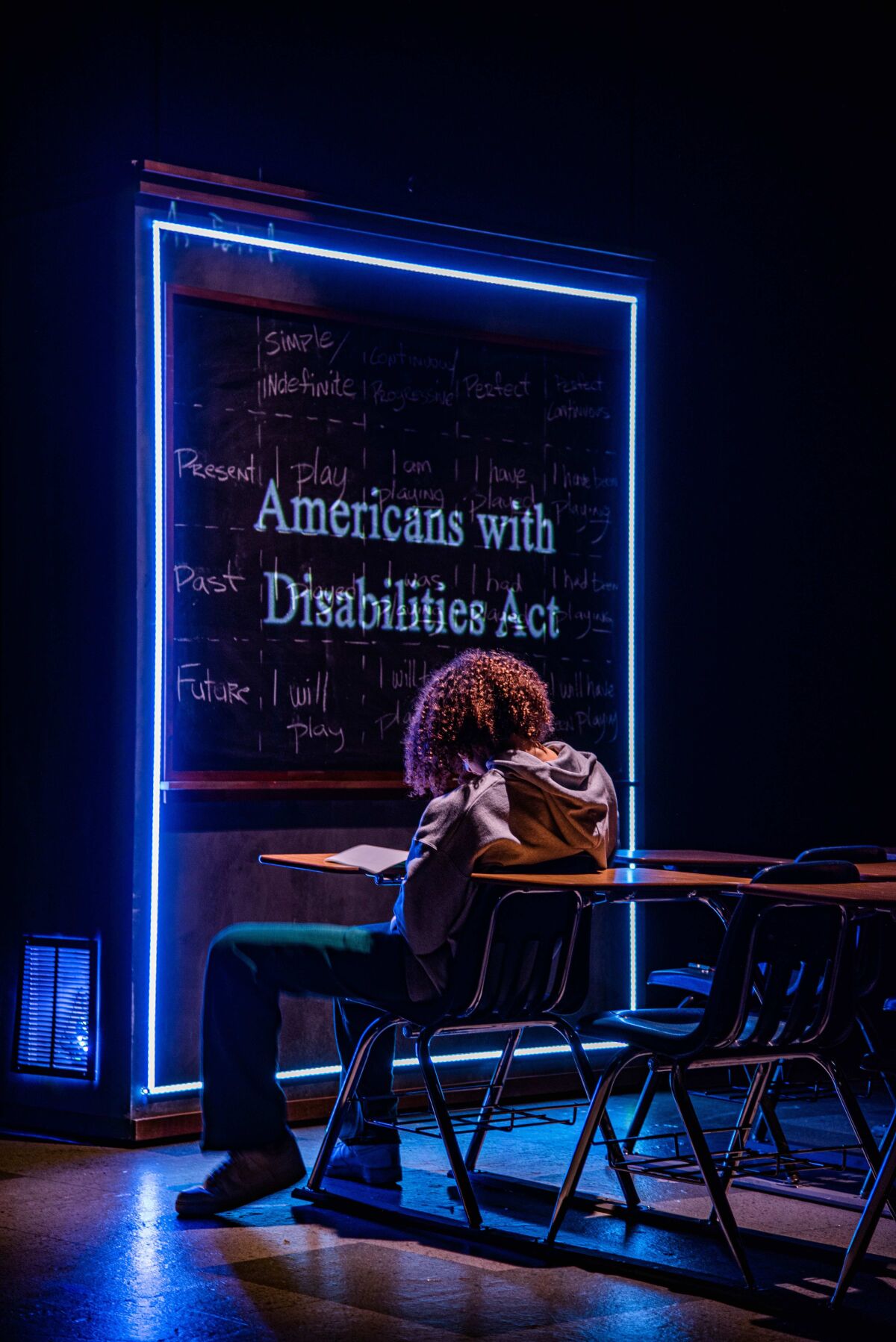 A young man sitting at a classroom desk with 'Americans with Disabilities Act' projected on the wall