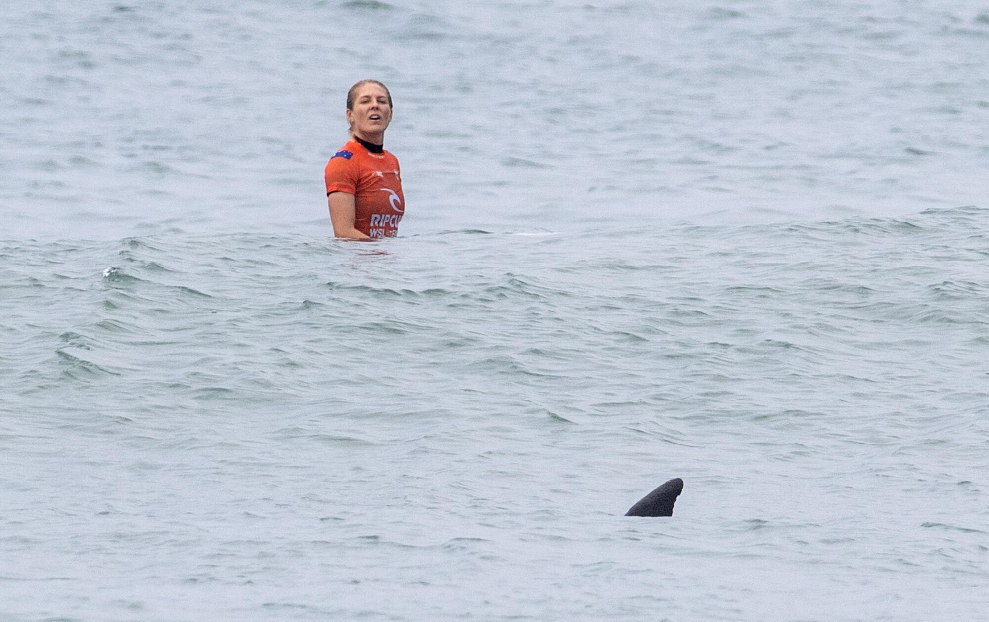 Stephanie Gilmore looks curiously at the fin of a dolphin swimming near her during a match at the WSL Finals.