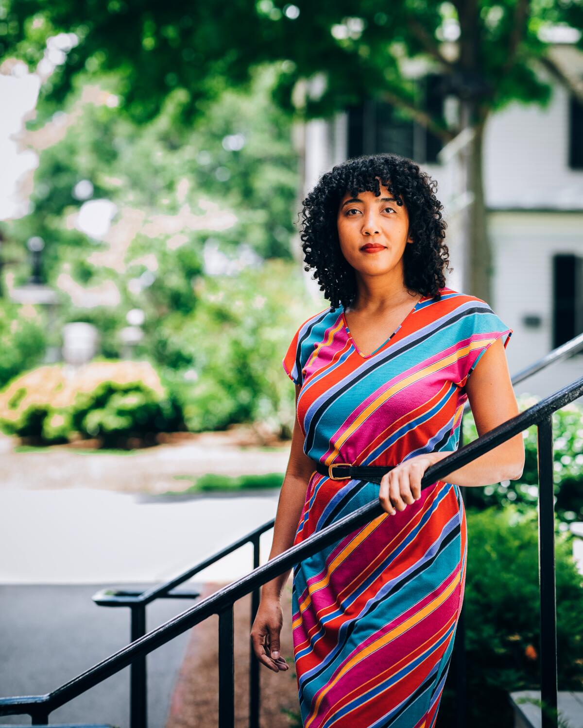 A woman in a diagonal striped dress poses on outdoor steps.