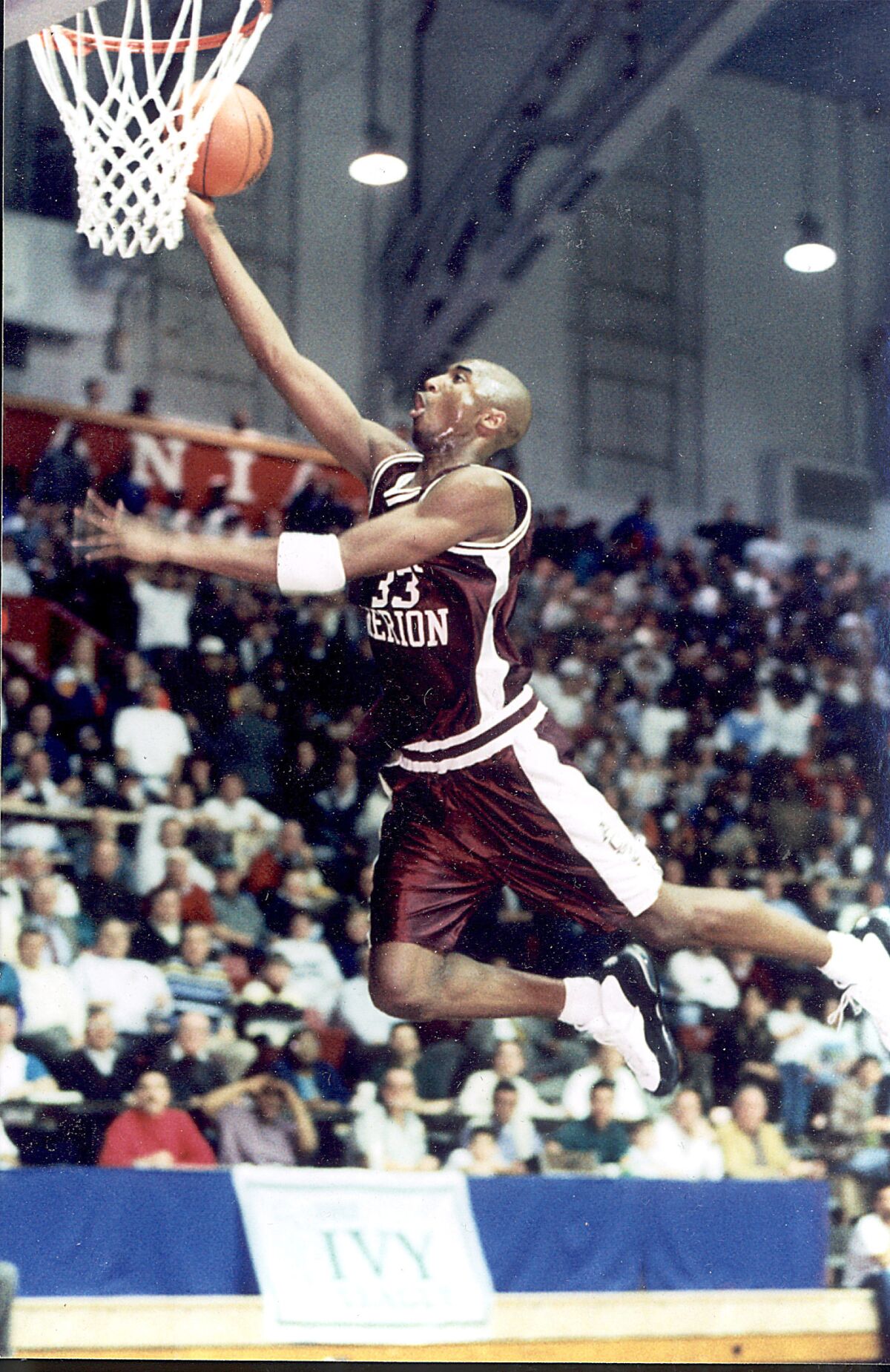 A mid-air shot of a basketball player reaching to the basket with the ball in one hand.