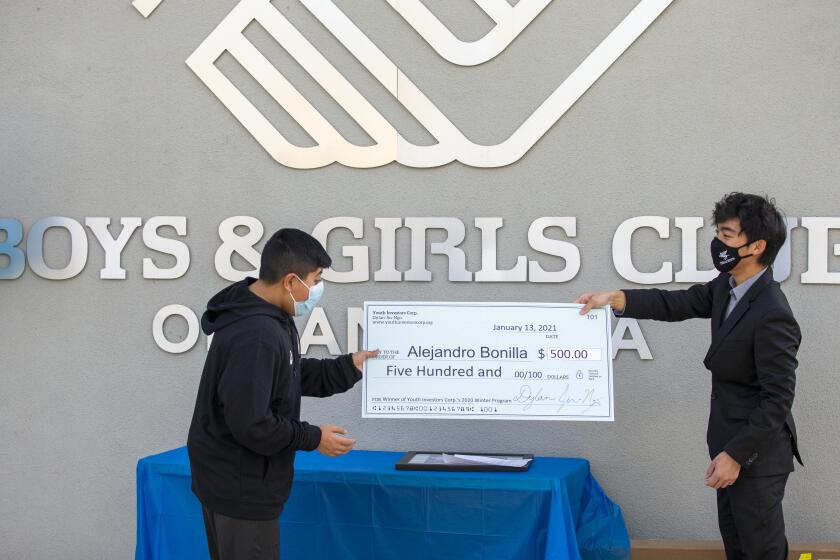 Alejandro Bonilla, 11, left, receives a check for $500 from Dylan Jin-Ngo, the founder of Youth Investors Corp., during an awards ceremony at the Boys & Girls Club of Santa Ana on Wednesday, January 9.