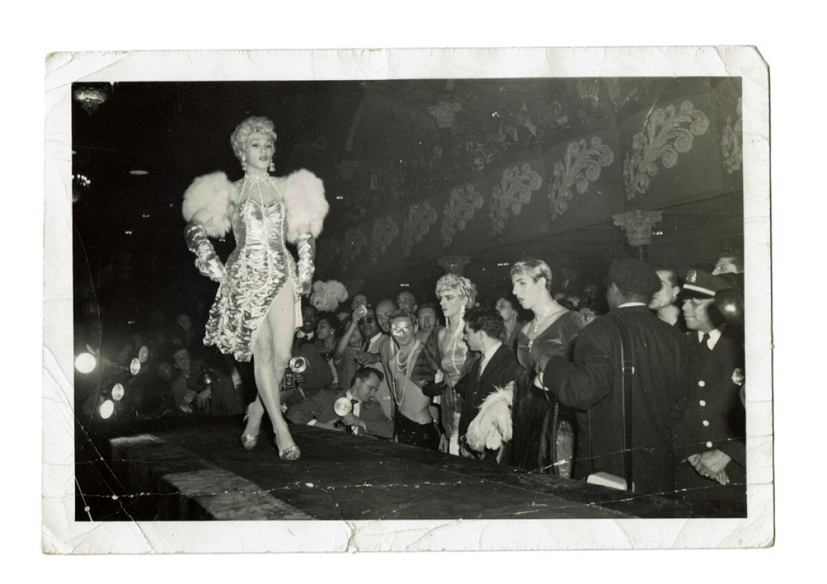 A drag queen walks a runway at a drag ball circa 1955