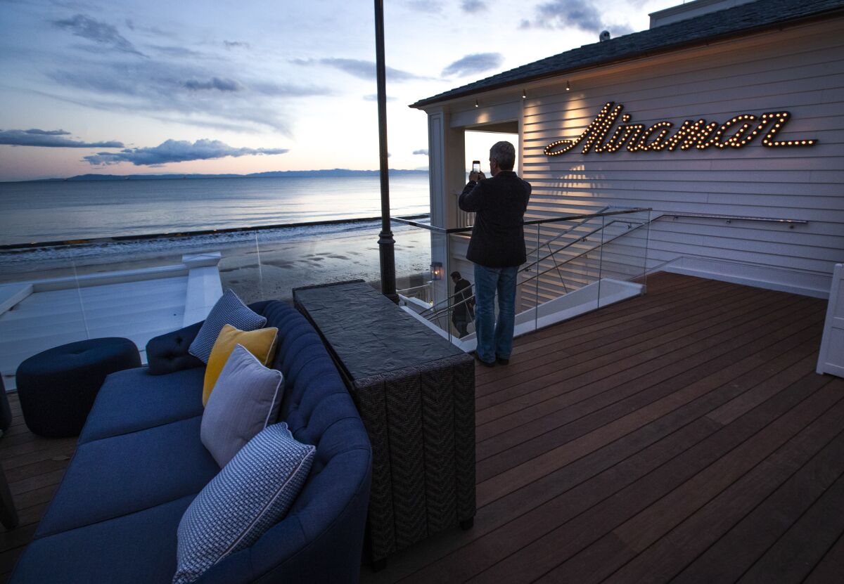 A man takes photos on the outdoor terrace of an oceanfront bar.