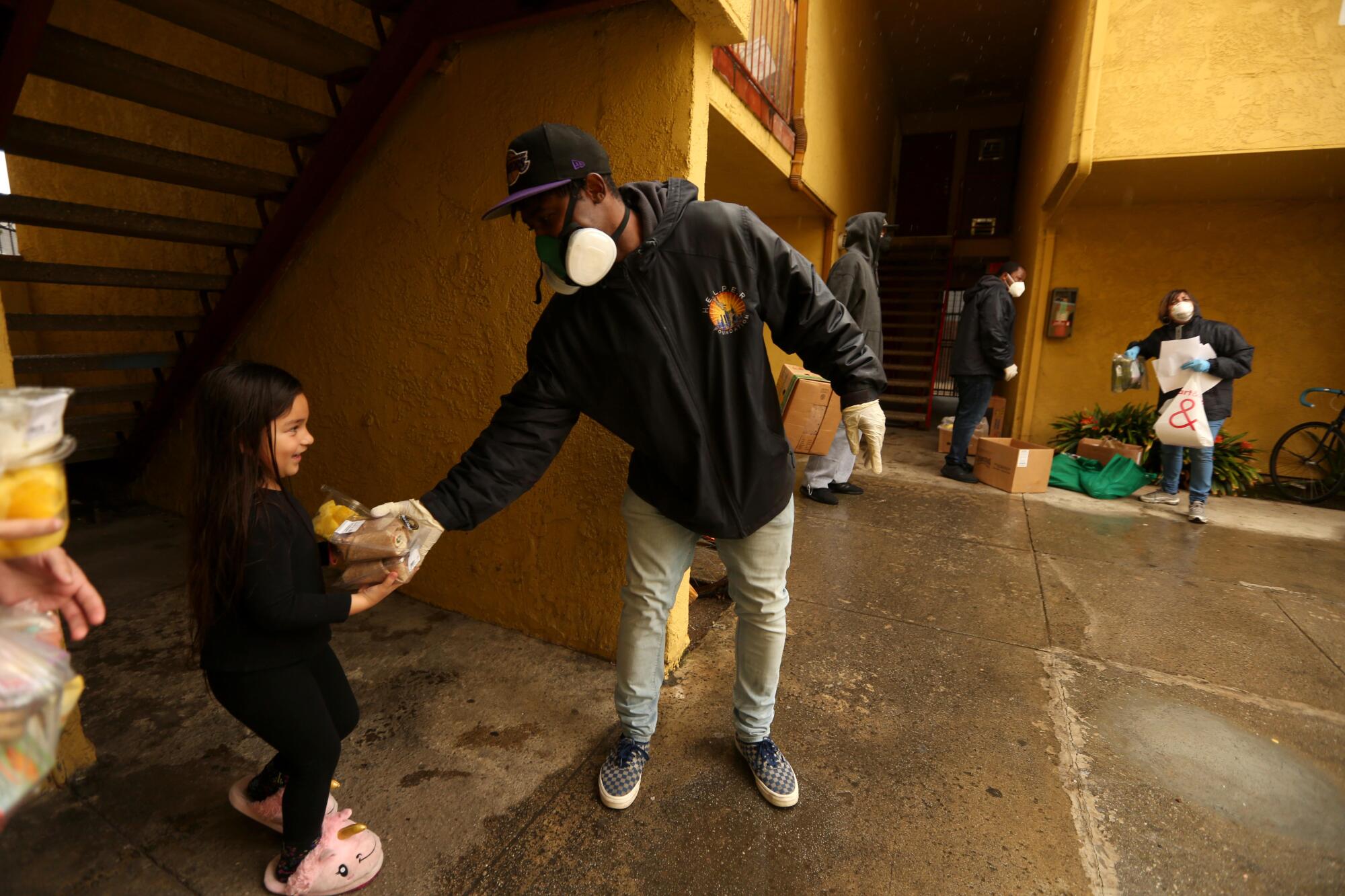 Ebay Williams, right, with the H.E.L.P.E.R. Foundation, gives a youngster and her family groceries at a low income government building in the Oakwood neighborhood in Venice.