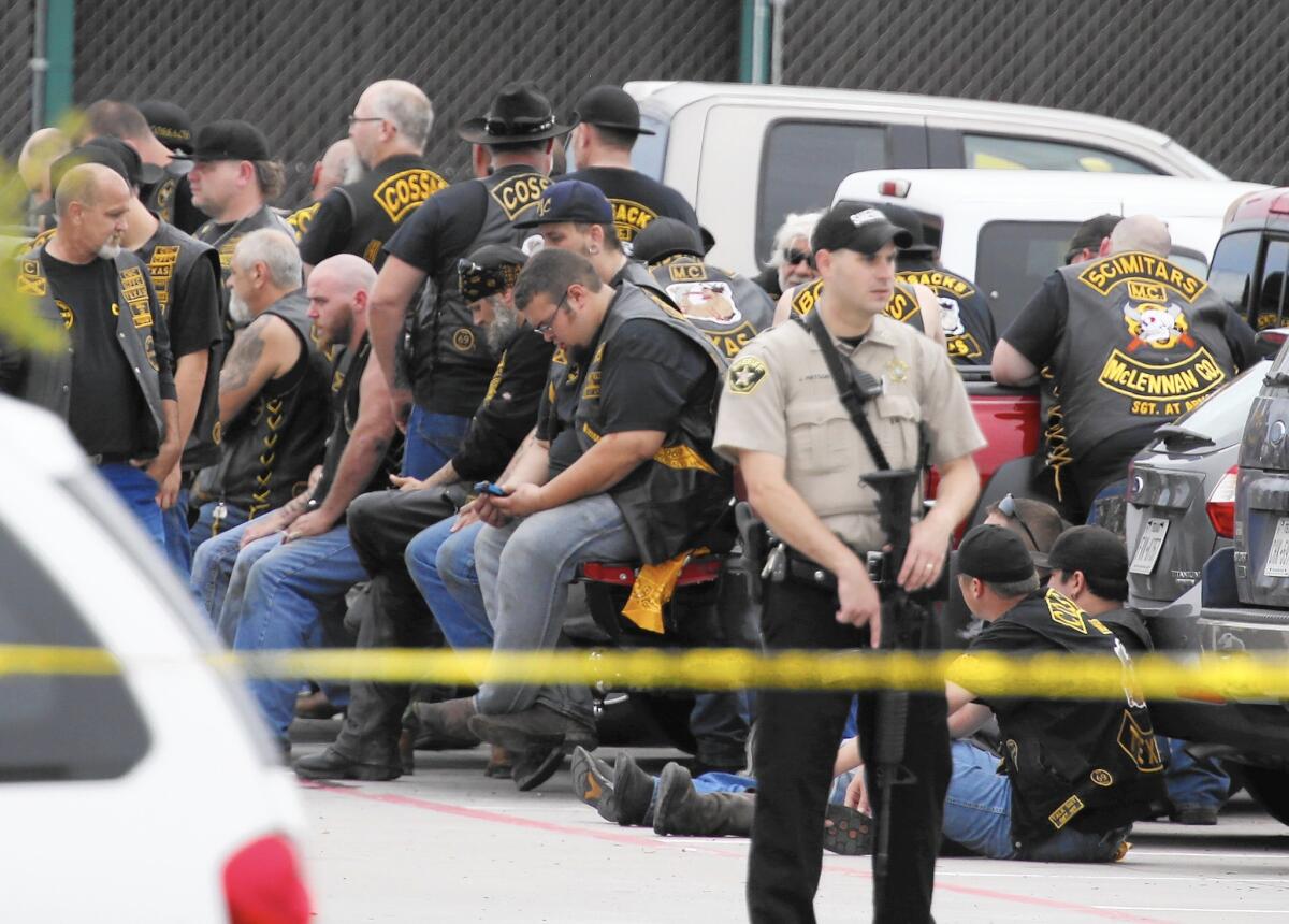 A McLennan County deputy stands guard near a group of bikers outside a restaurant in Waco, Texas, on May 17 after a shootout that involved two motorcycle gangs.