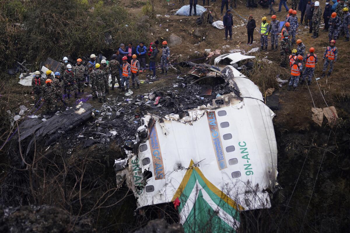 A view of workers in hard hats standing below, near the wreckage of a plane 