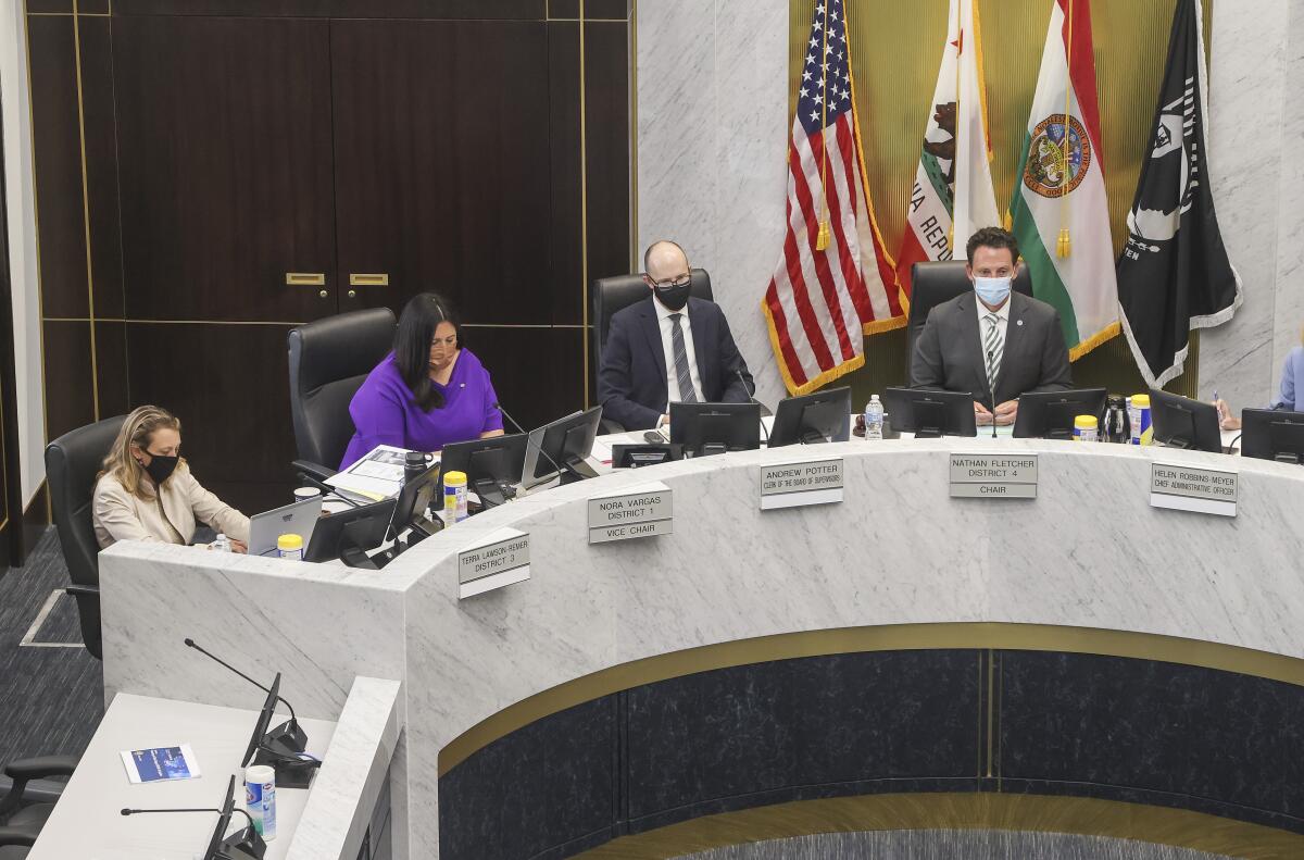 Four of the County Board of Supervisors in seats behind a U-shaped dais 