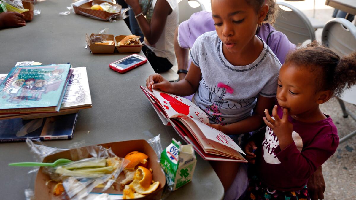 Princess West, 8, center, reads to her friend Mercy Cooper, 2, after the pair enjoyed a free lunch as part of the Summer Food Service Program at the Inglewood Public Library.