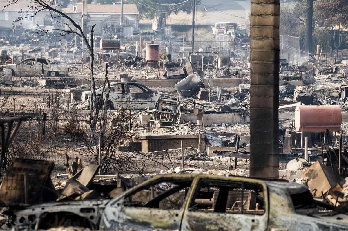 Burned vehicles and leveled homes fill a wildfire landscape.