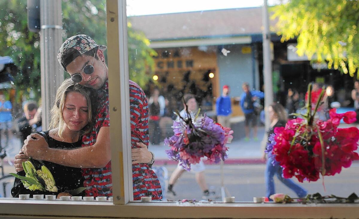 UCSB student Connor London gets a hug from fellow student Noel Peake after placing memorial flowers in the bullet holes in the front glass of the I.V. Deli Mart in Isla Vista.