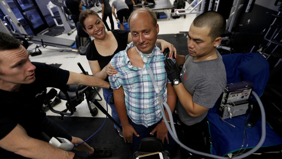 Physical therapy for diving coach Lenny Larson includes standing with the help of a team at NextStep Fitness in Lawndale.