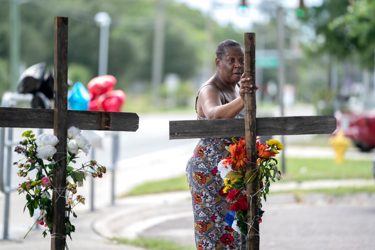 A Black woman touches a memorial in the shape of a cross that is draped with flowers