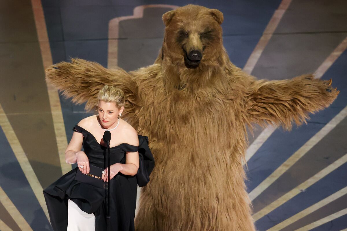 A woman in an evening dress standing next to a person in a bear costume