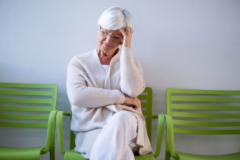 Tensed senior woman sitting on chair in waiting area of hospital