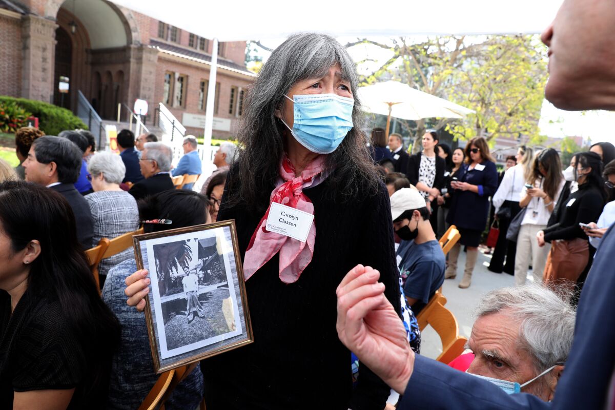 A person in a mask holds a framed black-and-white photo